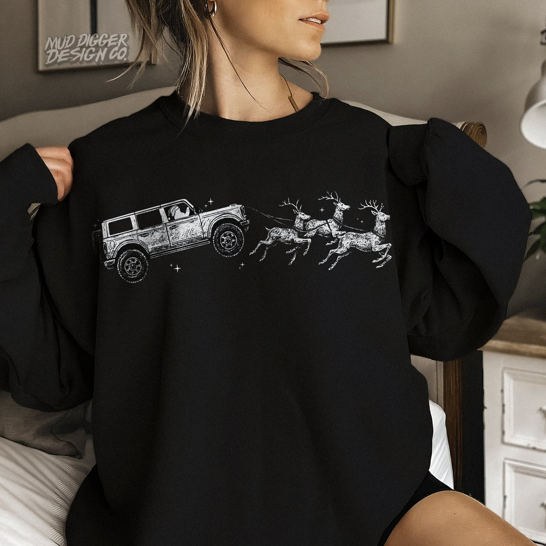 Black holiday crewneck featuring a Ford Bronco pulling Santa’s sleigh with reindeer – festive unisex Christmas sweatshirt by Mud Digger Design Co.