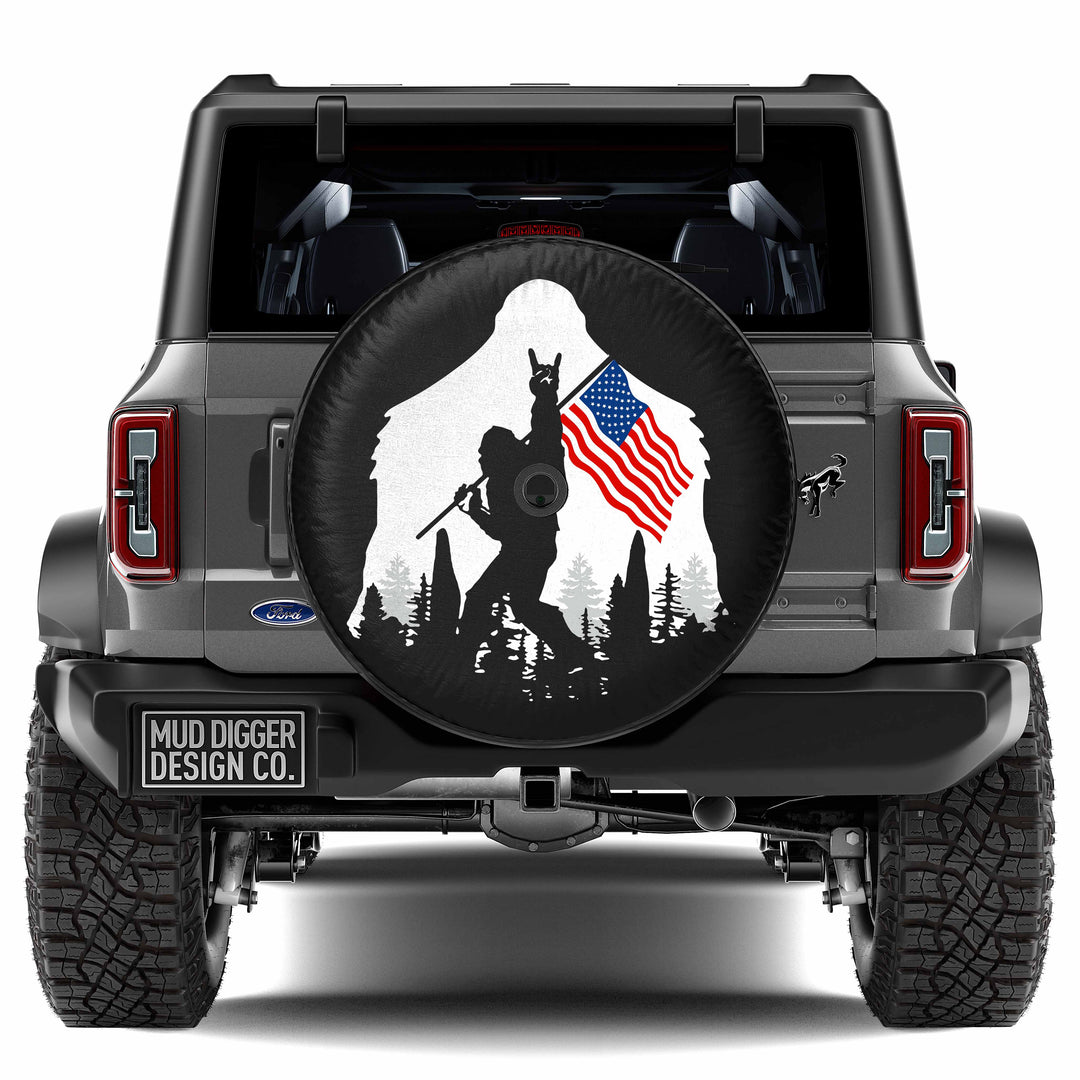 Ford Bronco Patriotic Sasquatch Tire Cover featuring a bold American flag design with a Bigfoot silhouette. Weather-resistant, durable, and custom-fit for Bronco spare tires—perfect for off-road and adventure enthusiasts.