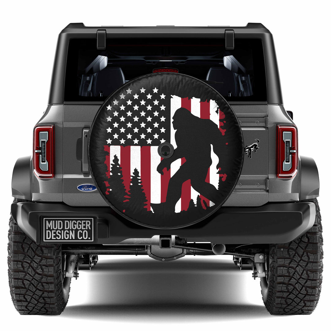 Ford Bronco Sasquatch Flag Tire Cover featuring a rugged design with an American flag and Sasquatch silhouette, perfect for off-road enthusiasts and adventure seekers. Durable, weather-resistant, and custom-fit for your Bronco